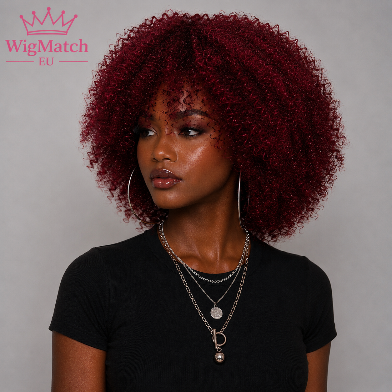 woman wearing a burgundy afro kinky curly human hair wig, looking 45 degrees to the left, with dark chocolate skin, a black top, and a soft light gray studio background wigmatch EU.
